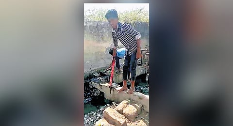 Students remove dirty water from a drain near the school at Kyatnal village of Yadgir