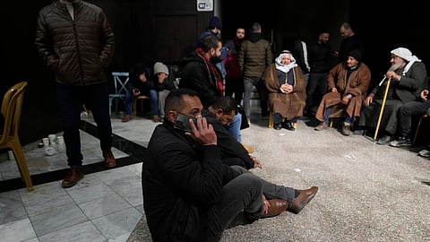 A man waiting for the release of Palestinian prisoners sits on the ground and uses his mobile phone Sunday, Feb. 23, 2025, after receiving news that Israel has delayed the release of hundreds of Palestinian prisoners scheduled for Saturday in the West Bank city of Ramallah.