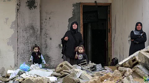 Women and children stand by the rubble of a collapsed building outside another building at the Shati camp for Palestinian refugees north of Gaza City on February 11, 2025.