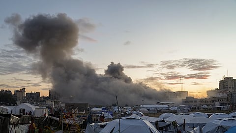 Behind a tent camp for displaced Palestinians, smoke rises from a building after it was targeted by an Israeli army strike, following evacuation orders for residents, in Gaza City, Saturday, March 22, 2025.