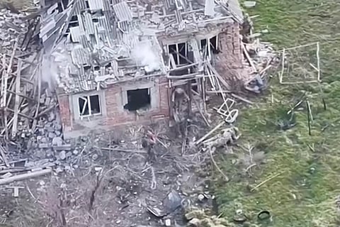 This image taken from video that European military officials say was filmed by a Ukrainian drone in the southern Ukrainian village of Piatykhatky on March 13, 2025, shows a soldier, left, identified as Russian, pointing his gun at a Ukrainian soldier who appears to be surrendering after emerging from the ruins of a house to join other Ukrainian prisoners on the ground.