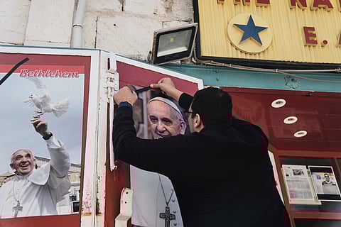 A shop owner places a black ribbon over a photo of the late Pope Francis after the news of his death at age 88, in Bethlehem, West Bank, on Monday, April 21, 2025.