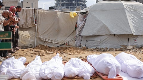 A boy peeks out of a displacement tent as Palestinians pray by the bodies of members of the Abou Mahadi family, killed in Israeli strikes on the family home in Beit Lahia, outside the Indonesian Hospital in the northern Gaza Strip on APril 28, 2025