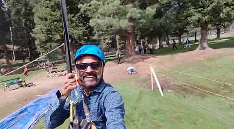 This screengrab from the video shows Rishi Bhatt on a zipline as people run in the background. 