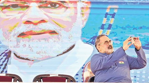 BJP state president Rajeev Chandrasekhar clicks a selfie while seated on the dais.