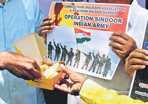 Citizens share a box of sweets and hold up posters celebrating the success of Operation Sindoor in Bengaluru on Wednesday