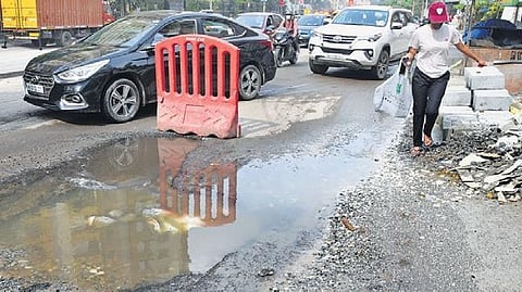 A pedestrian struggles to walk along the potholed Hennur road in Bengaluru. 