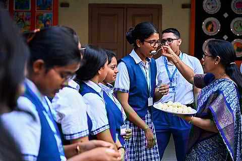 A teacher distributes sweets to students for passing CBSE plus two exams with flying colours at BJEM School in Bhubaneswar on Tuesday. 
