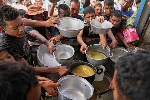Palestinians struggle to receive cooked food distributed at a community kitchen in Khan Younis, southern Gaza Strip, Wednesday, May 14, 2025.