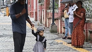 A child seeks refuge from a light drizzle, holding tightly to her father near the Mahatma Ayyankali Hall in Thiruvananthapuram on Sunday