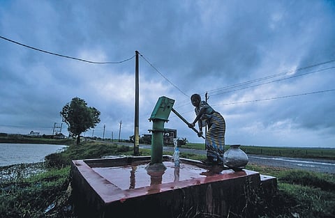 A woman collects water from a hand pump in the suburbs of Bhubaneswar, as dark clouds shroud the skyline, on Wednesday