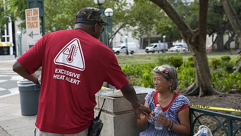 Ricky Leath, an outreach specialist with the City of Miami, talks with Bei Zhao, right, as he works with the Miami-Dade County Homeless Trust to distribute bottles of water and other supplies to the homeless population, helping them manage high temperatures, May 15, 2024, in Miami. 