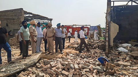 Police personnel and others stand at a firecracker manufacturing and packaging unit after a blast killed at least five migrant labourers and injured many others at a village, in Sri Muktsar Sahib district, Punjab.