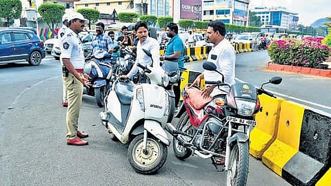 A traffic police officer detains two-wheeler riders without a helmet.