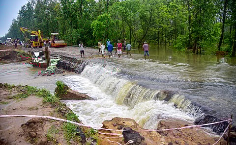 People stand as floodwater flows through a washed away portion of the National Highway 17 after heavy rainfall, in Kamrup district, Assam, Saturday, May 31, 2025.