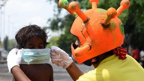 As a part of a Covid awareness campaign, a man gives a mask to a child.