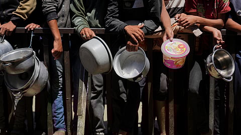 Holding their pots, Palestinians wait to get donated food at a community kitchen in Khan Younis, southern Gaza Strip, Monday, June 2, 2025.