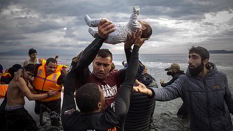 A volunteer holds up a baby as others help migrants and refugees disembark from a dinghy after their arrival from the Turkish coast to the Greek island of Lesbos on Nov. 25, 2015