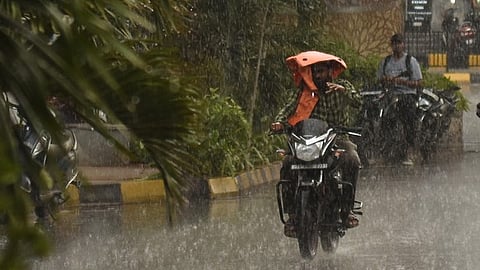 A man is covering himself from the rain while riding his bike at Somajiguda in Hyderabad. 