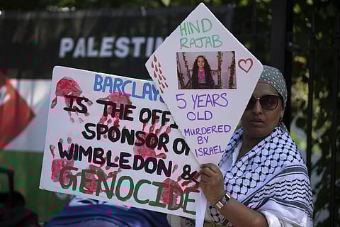 A protestor of the Palestine Solidarity Campaign against the tournament's sponsor Barclays holds posters outside the Wimbledon Tennis Championships in London, Monday, June 30, 2025.