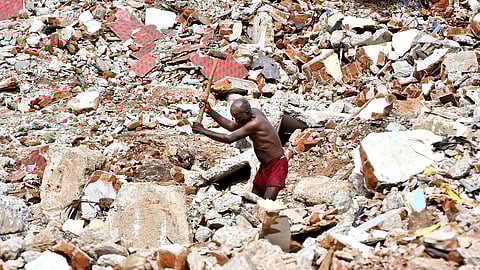 A daily wage worker toils amidst the ruins of a demolished building, hammering through debris under the harsh sun in Chennai