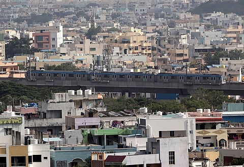 A Hyderabad Metro train passes through a dense maze of concrete structures, seen from Mahendra Hills in the city. 