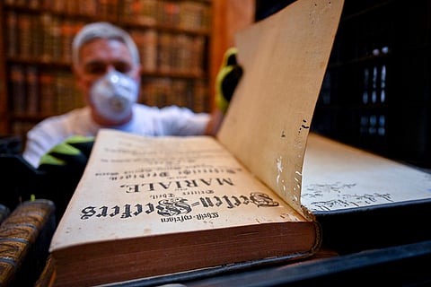 In this photo provided by Pannonhalma Archabbey, a restorer shows an old book with holes in its pages due to a drugstore beetle infestation, at the Pannonhalma Archabbey's library in Pannonhalma, Hungary, Thursday, July 3, 2025, as a beetle infestation threatens its ancient collection.