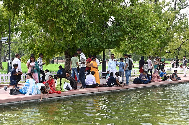 People sit along a pool of water on lawns of the Kartavya Path near India Gate on July 16, 2025, in New Delhi, as authorities ban picnics and eatables around Central Vista, maintaining appearances.