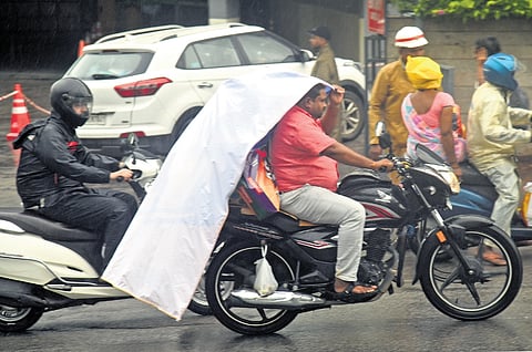 A motorcyclist shields himself from the drizzle using a plastic sheet in Hyderabad on Saturday