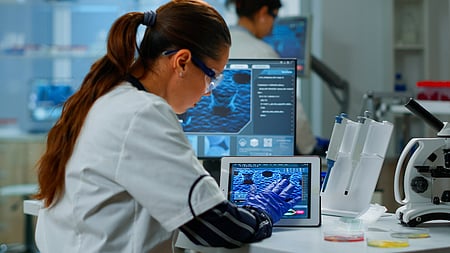 A scientist using a digital tablet working in a modern medical research laboratory, analysing DNA information.
