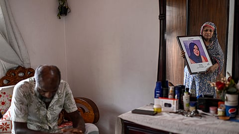 Asma Begum, standing next to her husband, is reflected in a mirror as she holds a portrait of her daughter Meherunnesa, who died by a stray bullet while standing near a window at her home, hours after former Prime Minister Sheikh Hasina fled the country amid a student-led mass uprising last year in Dhaka, Bangladesh, July 28, 2025. 