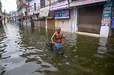 A man with his bicycle makes his way through a waterlogged area following rainfall, in Prayagraj, Uttar Pradesh, on Monday