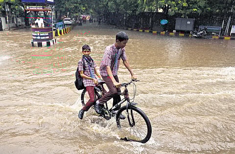 Students ride through a flooded road at Raj Bhavan on Monday.