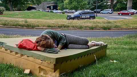 Stephanie W., 28, who is homeless, rests on a foam mattress as a United States Park Police vehicle drives past, Wednesday, Aug. 13, 2025, in northwest Washington near the Kennedy Center.