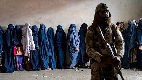 A Taliban fighter stands guard as women wait to receive food rations distributed by a humanitarian aid group, in Kabul, Afghanistan, Tuesday, May 23, 2023.