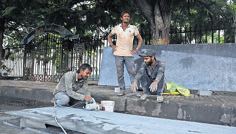 Workers cut stone slabs for an Indiramma Canteen on a pavement near the State Museum.
