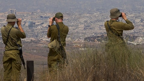Israeli soldiers uses binoculars to look at damaged buildings in the Gaza Strip, from southern Israel, Wednesday, Aug. 13, 2025.