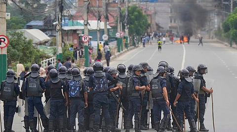 Policemen in riot gear stand guard on a street as protesters burn tires violating curfew orders in Kathmandu, Nepal, Tuesday, Sept. 9, 2025.