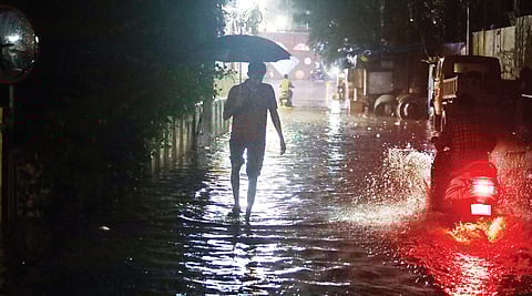 Amid rains, a man walks through a waterlogged road at Somajiguda in Hyderabad late on Sunday.