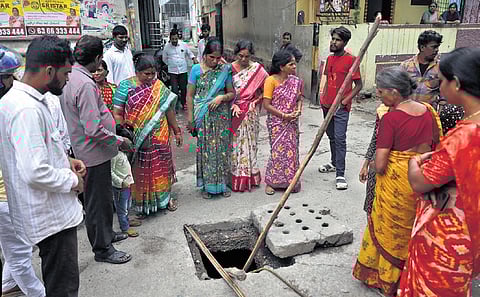 People gather around a manhole at Gangaputra Nagar in Secunderabad where the bike of a man washed away in a stormwater drain got stuck.