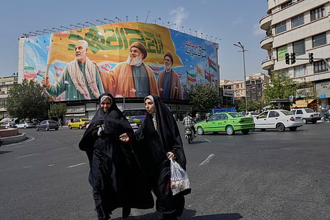 Two women walk past a huge banner showing the late commander of the Iran's Revolutionary Guard expeditionary Quds Force, Gen. Qassem Soleimani, who was killed in a U.S. drone attack in 2020, and two late Hezbollah leaders Hassan Nasrallah, center, and Hashem Safieddine, who were killed in Israeli airstrikes in 2024, at the Enqelab-e-Eslami (Islamic Revolution) square, in Tehran, Iran, Saturday, Sept. 27, 2025.