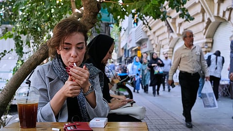A woman lights a cigarette in the alfresco dining area of a cafe at the Enqelab-e-Eslami (Islamic Revolution) street, in Tehran, Iran, Saturday, Sept. 27, 2025.