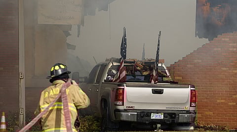 A vehicle that was rammed into the building is surrounded by smoke as a firefighter works on the scene at the Church of Jesus Christ of Latter-day Saints in Grand Blanc, Mich., Sunday, Sept. 28, 2025.