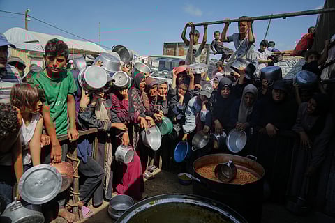 Palestinians wait to get donated food at a community kitchen in Khan Younis, southern Gaza Strip, Sunday, Oct. 5, 2025. 
