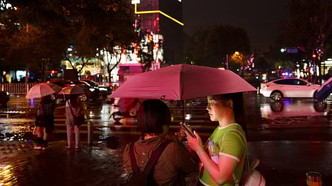 People look at their phones while waiting to cross an intersection in the rain at the Taikoo Li Sanlitun shopping center in Beijing, July, 30, 2024.