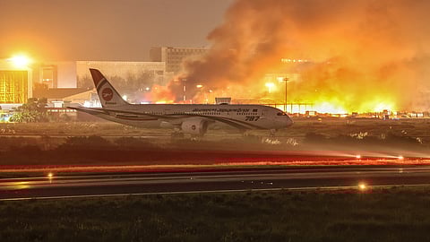 An airline plane stands on the tarmac as firefighters try to extinguish a fire that broke out in the cargo section of Hazrat Shahjalal International Airport in Dhaka on October 18, 2025. 