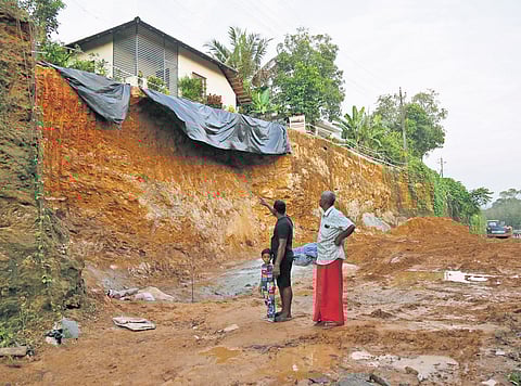 A house hangs precariously over the edge of the slope where the bypass works are progressing at Kollikkadu, Kothamangalam; residents walk through the bypass construction site where the mudslip occurred 