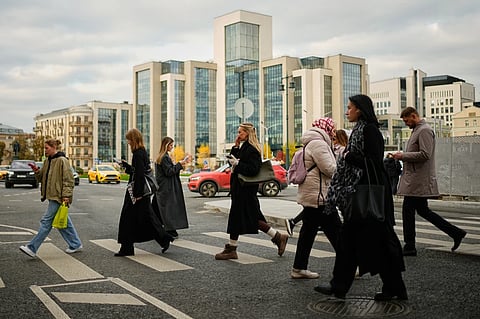 People cross a street, with Russian oil company Lukoil’s headquarters seen in the background, in Moscow, Russia, Thursday, Oct. 23, 2025. 