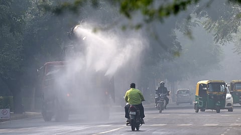 Commuters ride past an anti-smog gun spraying water to curb air pollution amid heavy smog conditions at Chanakya Puri in New Delhi.