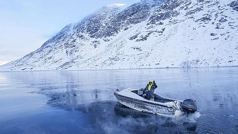 A fisherman rides on a boat though a frozen sea inlet outside of Nuuk, Greenland